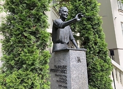 Pomnik na postumencie Tadeusz Sygietyńskiego przed Pałacem Karolin, wokół zieleń krzewów.