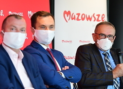 Zdjęcie z bliska. Trzech mężczyzn w maskach ochronnych siedzi obok siebie
