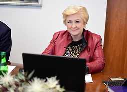 Członek zarządu Elżbieta Lanc siedzi przy stole przed otwartym laptopem