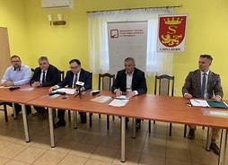 Pięciu uczestników spotkania siedzi za stołem na tle banerów z logotypami samorządu Mazowsza i Sierpca.