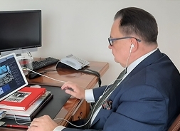 Ujęcie z boku, Marszałek siedzi w gabinecie za biurkiem przed laptopem, patrzy w ekran.