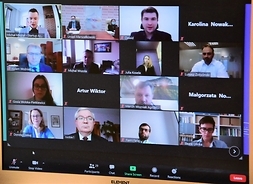 Ekran komputera a na nim stopklatka pokazująca okienka z kilkunastoma uczestnikami spotkania online.