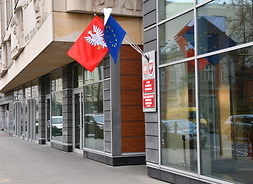Widok wejścia do urzędu marszałkowskiego, przy którym są uczepione flagi UE, Polski i Mazowsza
