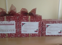 Trzy ładnie zapakowane kartony z darami, na pudełka naklejone są życzenia świąteczne