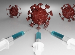 Trzy strzykawki leżą na stole skierowane w kierunku trzech kul, symbolizujących komórki wirusa