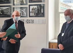 Wicemarszałek Raboszuk i dyrektor urzędu stoją przed ustępującym dyrektorem i wręczają mu list okolicznościowy.