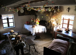 Wnętrze chaty w skansenie. Stoły zastawione są tradycyjnymi daniami, a izba przyozdobiona