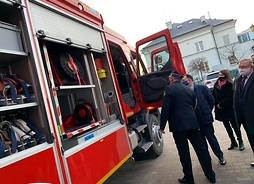 Bok samochodu strażackiego z otwartymi schowkami na sprzęt. Marszałek zagląda do wnętrza auta