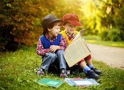 dwóch chłopców siedzi na skraju lasu i czyta książkę