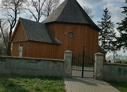 Drewniany kościół z bramą wiazdową i wybrukowanym wjazdem