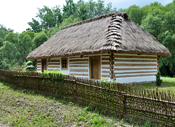 Wiejska chata kryta strzechą, otacza ją drewniany płot