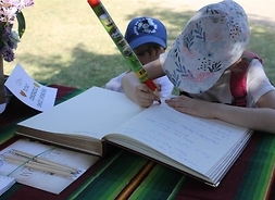 Dziecko wpisuje się do księgi pamiątkowej. Zdjęcie w plenerze.