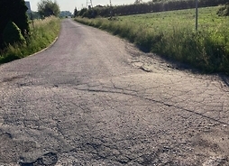 Popękany asfalt na wiejskiej drodze, w nawierzchni widać nierówności i dołki