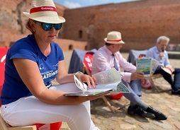 Na dziedzińcu zamku w Ciechanowie na leżakach siedzą uczestnicy konferencji, na pierwszym planie kobieta w słomkowym kapeluszu przegląda przewodnik turystyczny