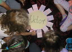 Grupa dzieci pochylona nad kartonem z napisem aktor i przyklejonymi do niego karteczkami