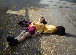 Dwie aktorki leżące jedna na drugiej na chodniku