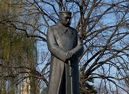 Spiżowy monument marszałka w charakterystycznym płaszczu. W tle duże drzewo