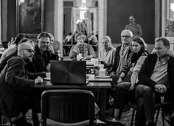 Grupa aktorów i reżyser siedząca przy stole i patrząca się w komputer przenośny