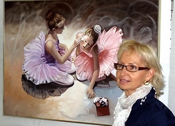 Malarka na tle jednego ze swoich obrazów, przedstawiających dwie młode baletnice