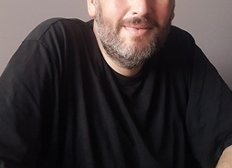Zdjęcie aktora – mężczyzny w średnim wieku, łysego i z siwą brodą i wąsami – w czarnym tshircie