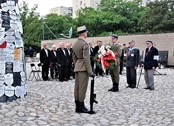 Zdjęcie przedstawia delegację składającą wieniec. Na pierwszym planie stoi żołnierz na warcie