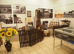 Zdjęcie przedstawia fragment wystawy: fotografie z życia mieszkańców wsi oraz przedmioty codziennego użytku, którymi się posługiwali, takie jak m.in. gliniane naczynia