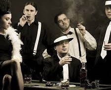 Muzycy zespołu Al Capone Band w strojach scenicznych. Cztery osoby stoją, jedna siedzi przy stole hazardowym