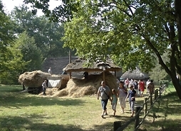 Zdjęcie przedstawia grupę zwiedzających radomski skansen idących wśród drewnianych zabudowan muzeum