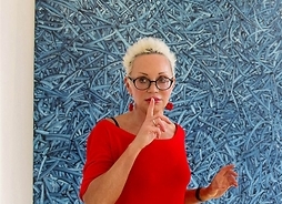 Kobieta w okularach z krótko ostrzyżonymi włosami, trzyma palec wskazujących przy ustach