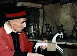 Mężczyzna w kapeluszu trzymający w dłoniach drewnianą rzeźbę przedstawiającą konia. Zdjęcie wykonane w pracowni artysty.